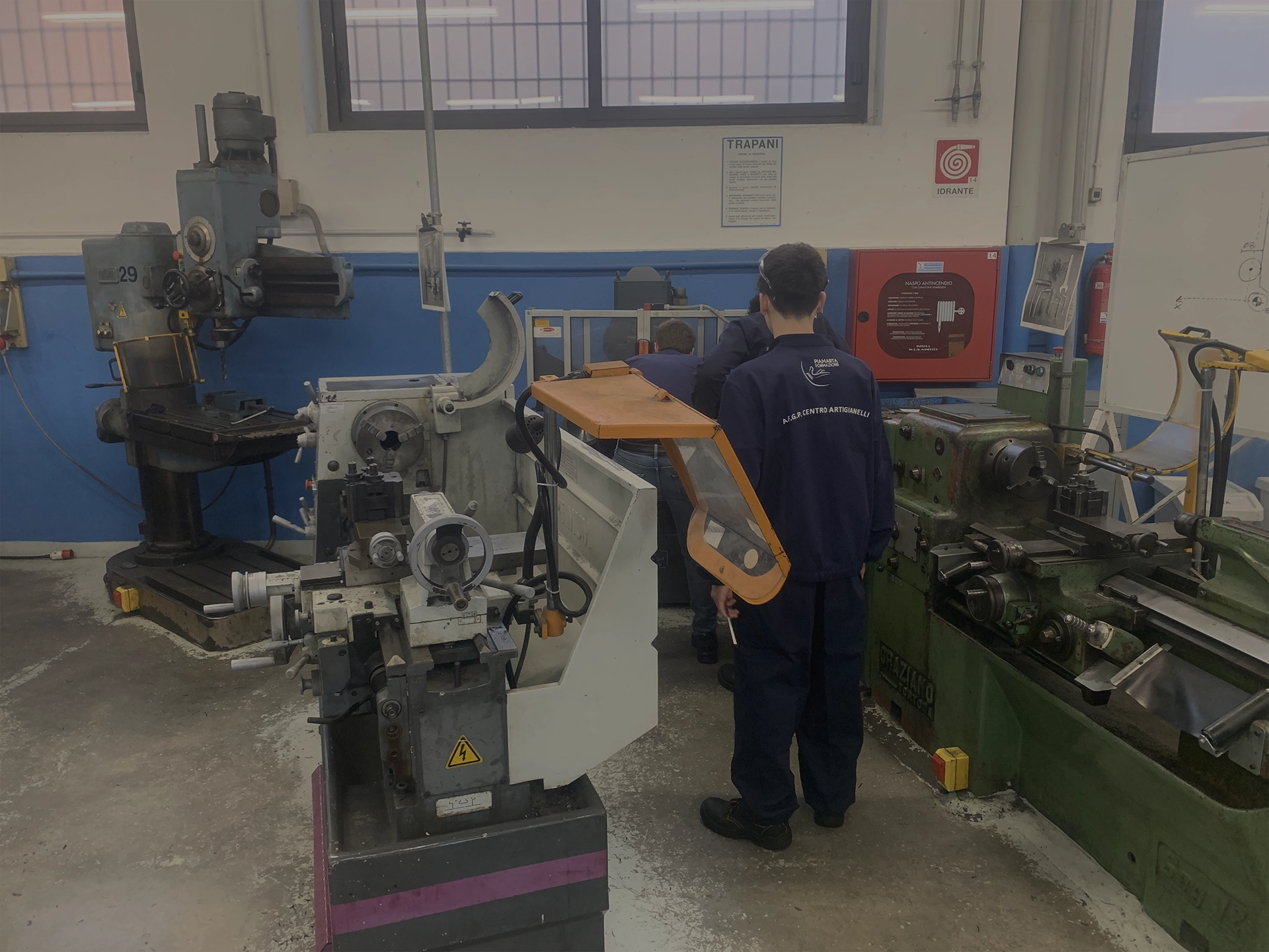  Un gruppo di studenti in un laboratorio meccanico, con macchine utensili come torni e trapani, impegnati in esercitazioni pratiche.