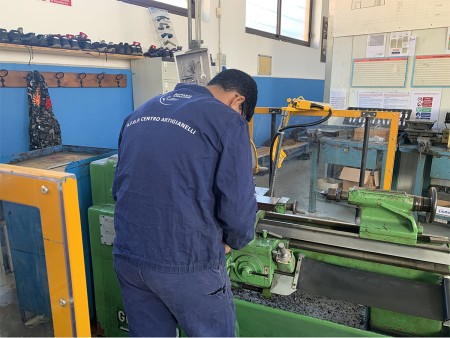 Studente in tuta da lavoro utilizza un tornio meccanico all'interno di un laboratorio, indossando abbigliamento protettivo.