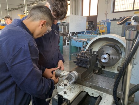 Studenti che utilizzano un tornio manuale in laboratorio, indossando occhiali di protezione.