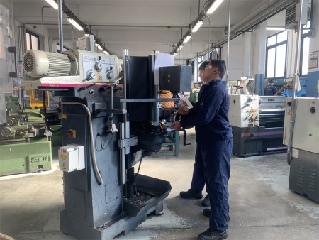 Studente in tuta da lavoro opera su una macchina utensile nel laboratorio, indossando occhiali di protezione.
