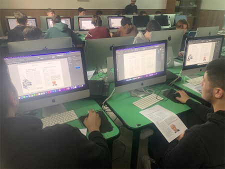 Studenti in aula informatica che lavorano su computer con Adobe InDesign, impegnati nell'impaginazione di articoli.