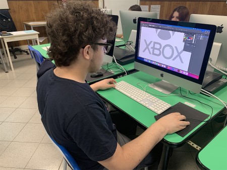 Studente che lavora al computer su un progetto di grafica con il logo Xbox, utilizzando un software di design.