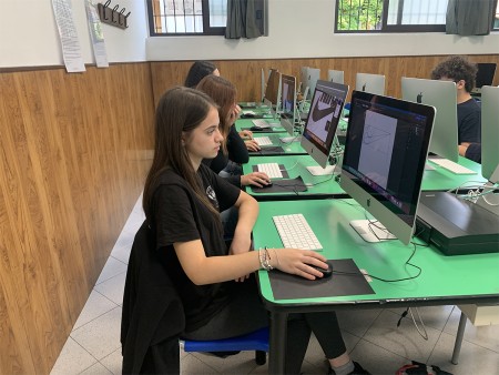 Studentessa al computer durante una lezione di grafica, con un progetto visibile sullo schermo.