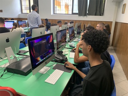 Studenti in aula informatica che lavorano al computer durante una lezione di grafica, con l'insegnante presente nella stanza.