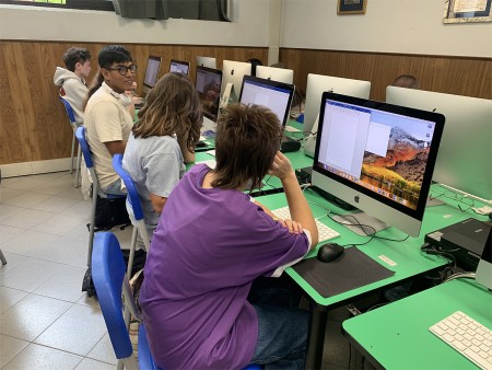 Studenti seduti davanti ai computer in un'aula informatica, impegnati in attività di scrittura e progettazione.