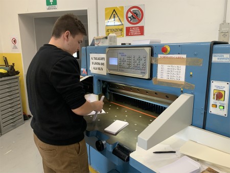 Studente utilizza una taglierina industriale per tagliare dei fogli di carta in laboratorio.