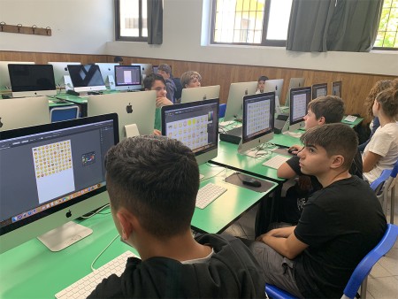 Studenti in aula informatica lavorano su computer con schermi che mostrano grafiche di emoji.