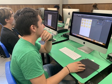Studente al computer in aula informatica, lavora su un progetto grafico con emoji.