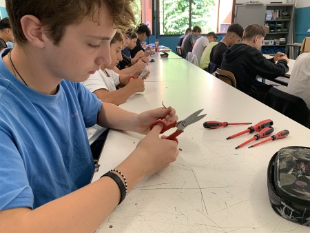 Studente usa le forbici per un'attività pratica, con cacciaviti sul tavolo.