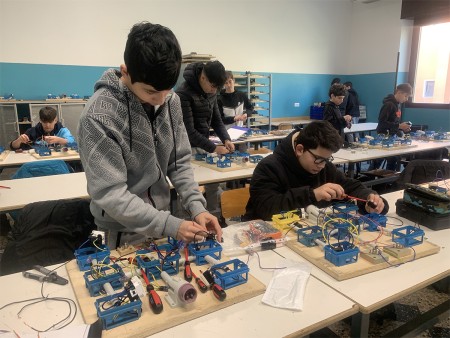 Studenti che lavorano su progetti elettrici in classe, assemblando componenti su pannelli di legno.