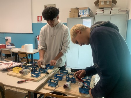 Due studenti montano circuiti elettrici su pannelli durante un'attività di laboratorio.