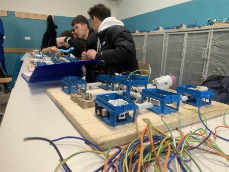 Studenti al lavoro su un progetto di cablaggio elettrico, con componenti e cavi in primo piano.