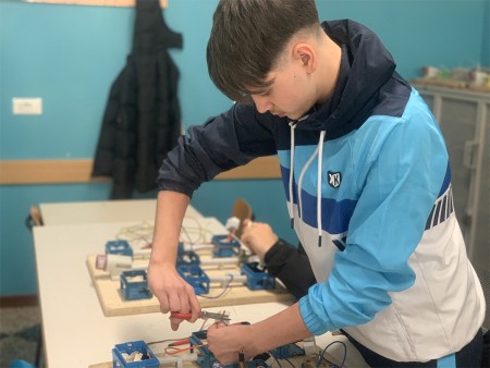 Studente impegnato nel montaggio di un circuito elettrico, utilizzando pinze per lavorare sui cavi.