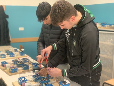 Due studenti eseguono cablaggi elettrici su un progetto scolastico, utilizzando pinze per collegare i fili.