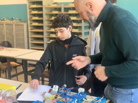  Studente che riceve indicazioni dall'insegnante su un progetto di cablaggio elettrico, con schemi e componenti sul tavolo.