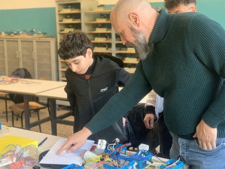  Studente e insegnante discutono un progetto di cablaggio elettrico, con l'insegnante che indica uno schema sul tavolo.