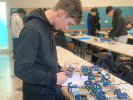 Studente lavora su un progetto di cablaggio elettrico, manipolando dei componenti elettrici su una tavola di montaggio.