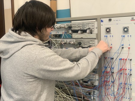 Uno studente lavora su un pannello elettrico, collegando vari cavi colorati, probabilmente durante un'attività di laboratorio tecnico o di automazione.