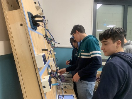 Studenti lavorano su un pannello elettrico, installando cavi e componenti, impegnati in un'attività pratica in laboratorio.