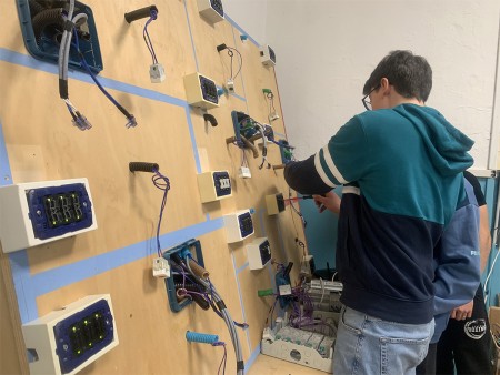Due studenti lavorano su un pannello elettrico, collegando cavi e componenti.