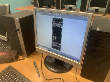 Un computer mostra un disegno tecnico realizzato con un software CAD, probabilmente parte di un progetto ingegneristico o di design tecnico. Accanto al computer c'è un astuccio e una penna.