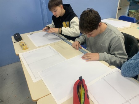  Due studenti concentrati usano un righello per disegnare linee precise su fogli bianchi. Sulla scrivania ci sono materiali come astucci e strumenti di disegno tecnico.